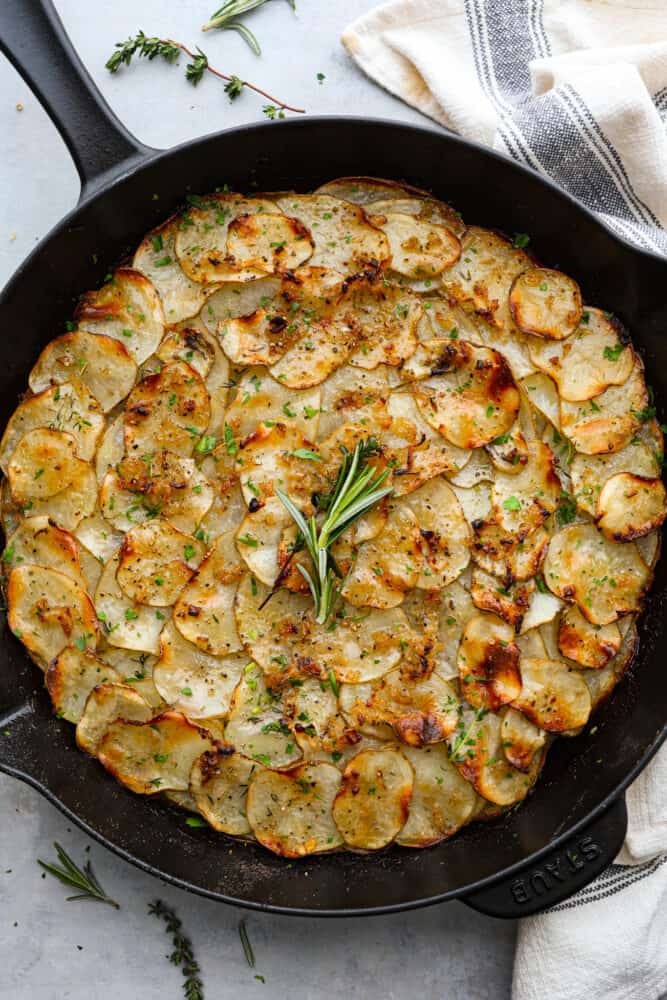 An overhead view of potato galette in a cast iron skillet with fresh herbs on top.