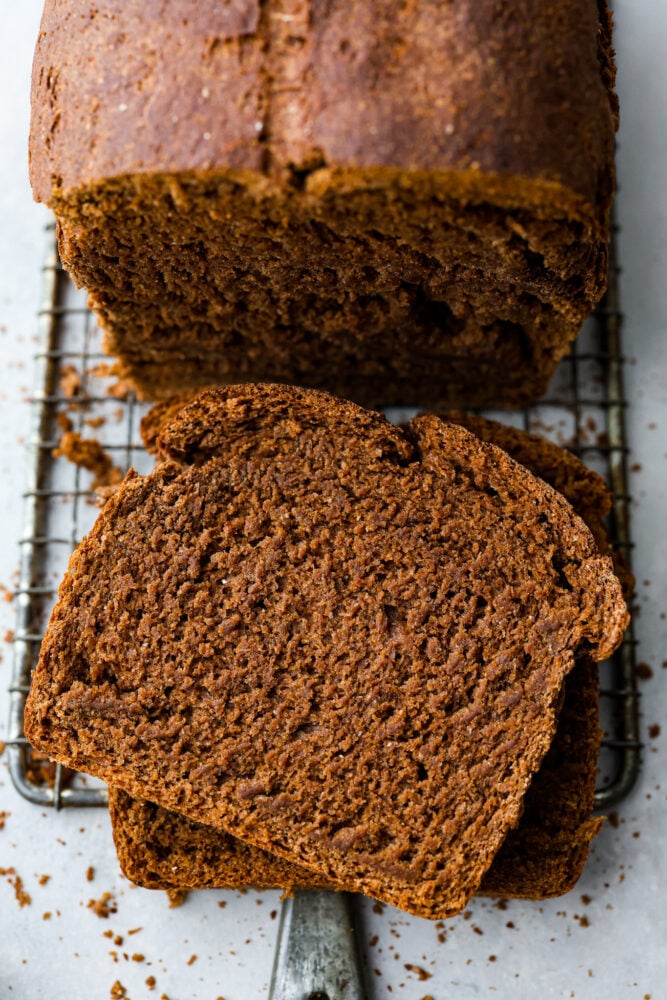 An overhead look at the loaf of pumpernickel bread with a few slices cut off on top of a wire rack.