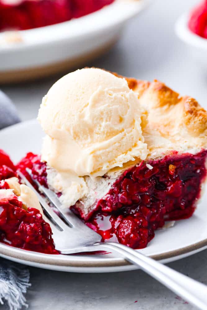 Raspberry pie is a timeless dessert that has been enjoyed for generations, and for good reason. With its flaky, buttery crust and tangy-sweet filling bursting with fresh, juicy raspberries, it’s the perfect balance of flavors and textures. And while store-bought options are convenient, nothing beats making it from scratch! Closeup of slice with a bite taken out of it.