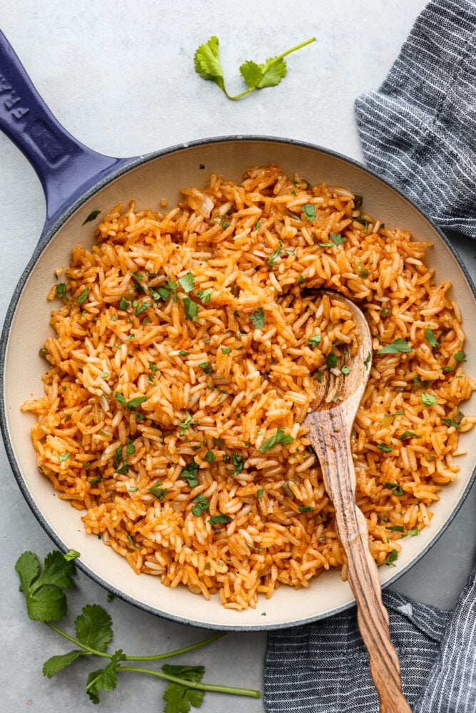 This Spanish rice delivers warm and exciting flavors that complement any meal! This tastes just like your favorite restaurant rice and is delicious served with any protein or Spanish inspired dish. Spanish rice in a skillet with a wooden spoon in it.
