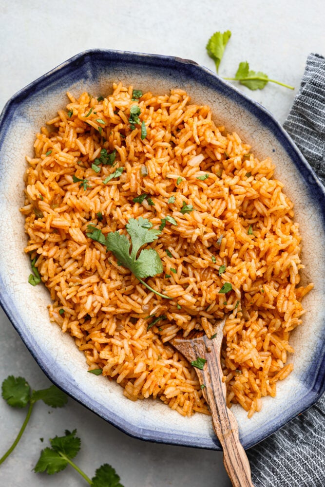 Spanish rice in a serving dish with a wooden spoon and fresh cilantro on top.