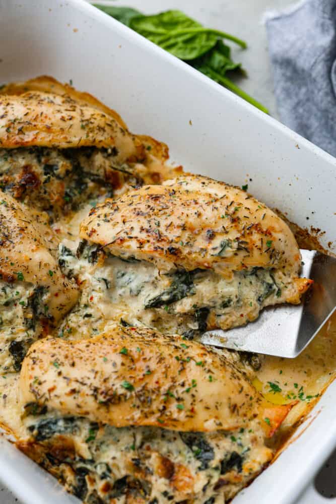 Spinach stuffed chicken breast in a pan with a spatula lifting up one of the breasts.