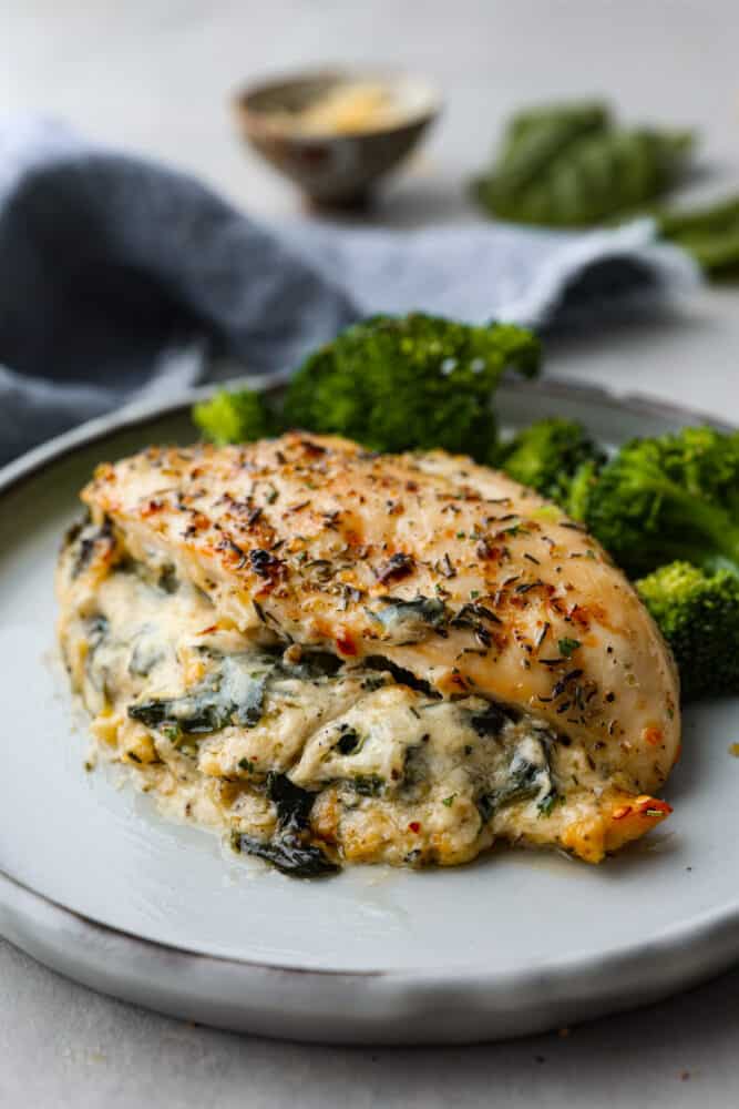 Spinach stuffed chicken breast on a plate with broccoli.