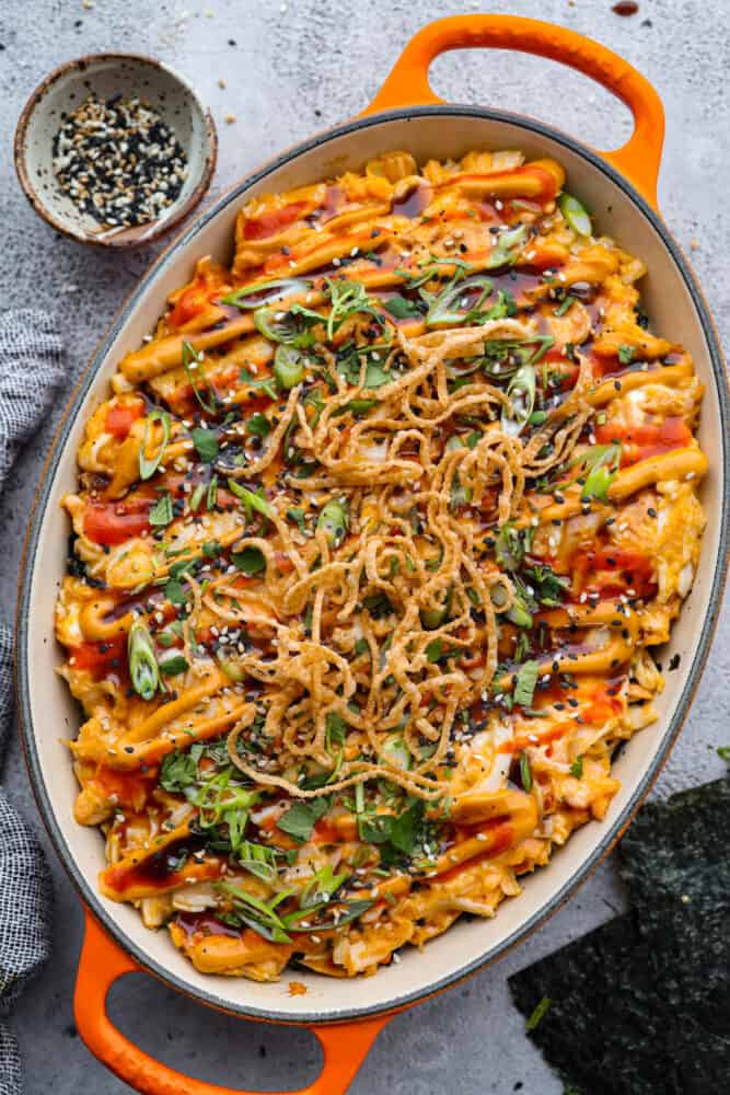 Sushi bake in an orange casserole dish with sesame seeds off to the side.