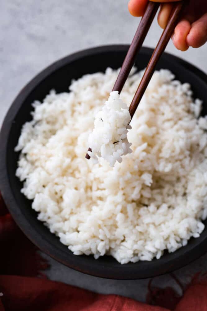 A hand holding chopsticks and taking a scoop of sushi rice.