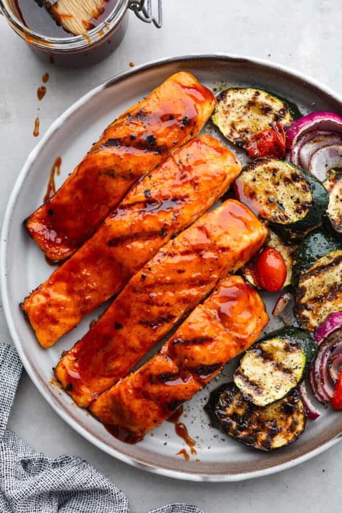 Top-down view of BBQ salmon on a white plate served with roasted zucchini.