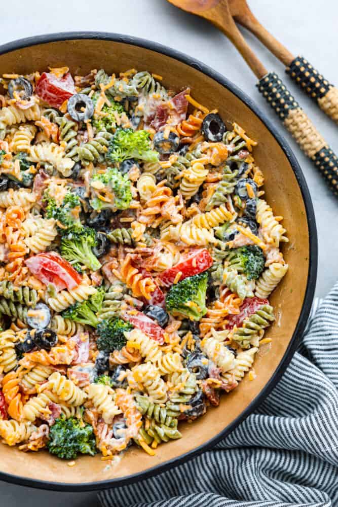 A bowl filled with bacon ranch pasta salad and 2 wooden spoons next to it. 