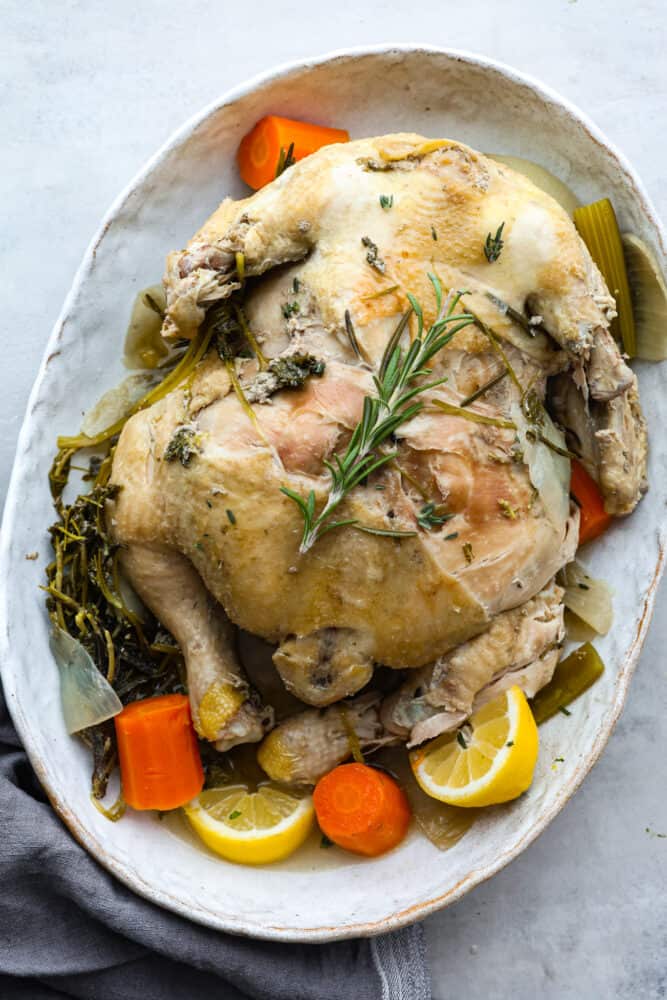 A whole cooked chicken served with vegetables on a white serving dish.