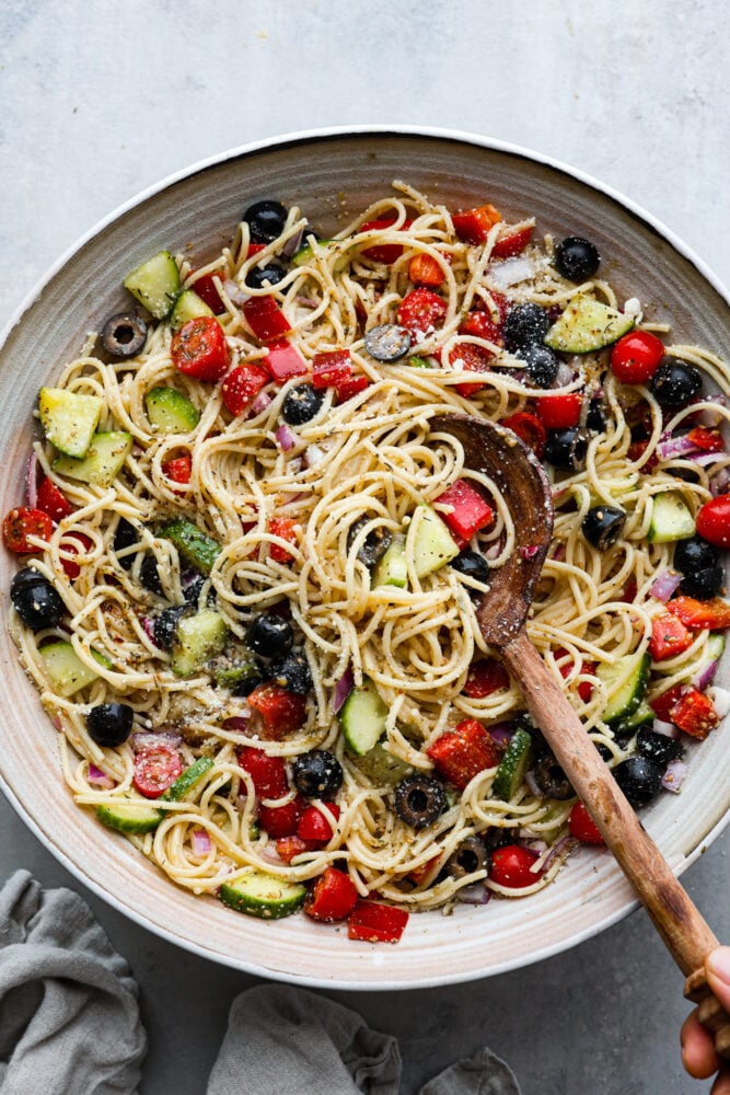 The top view of spaghetti pasta salad in a bowl with a wooden spoon. 