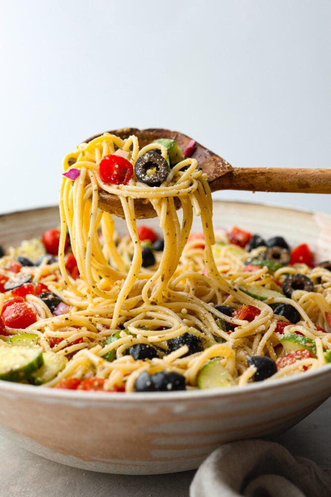 Side view of a bowl of pasta salad scooped out with a wooden spoon. 