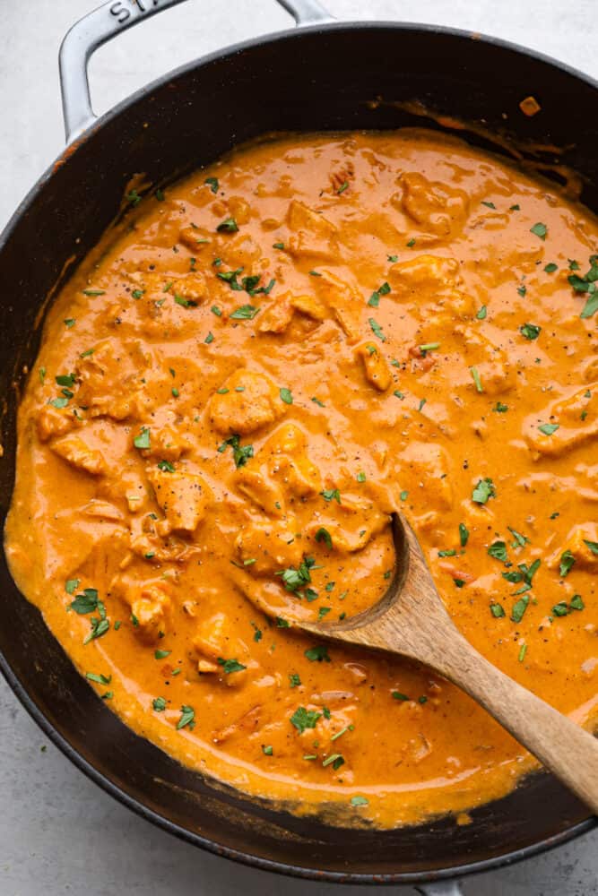 The top view of chicken paprikash in a pan with a wooden spoon. 