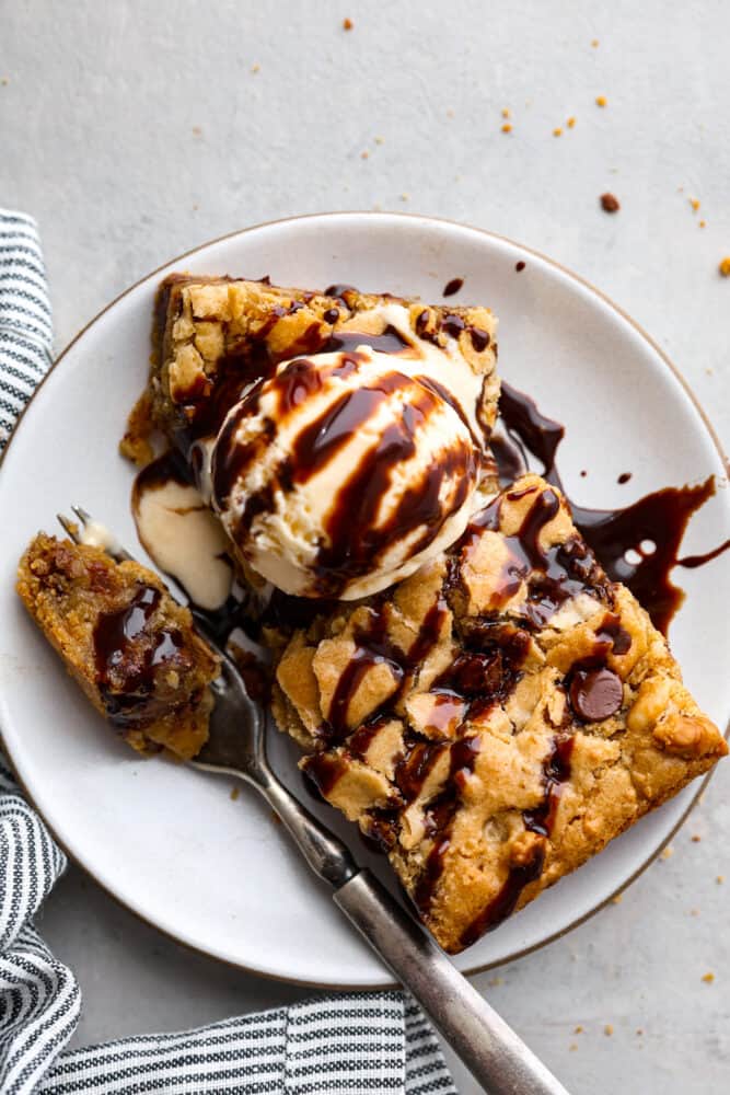 Congo bars are soft and chewy, filled with chocolate chips and walnuts. They’re like a gooey chocolate chip cookie in bar form and will have you savoring every bite! Top-down view of a congo bar slice served with vanilla ice cream and a drizzle of chocolate syrup.