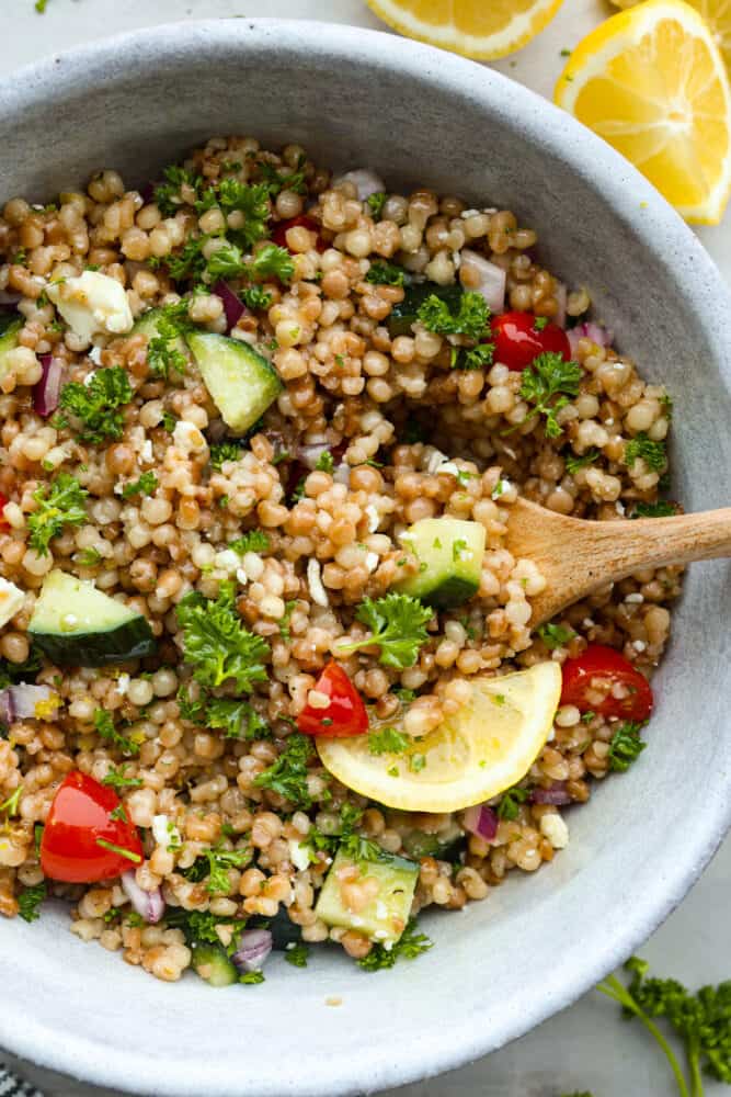 Closeup of pearl couscous salad, made with fluffy couscous, cucumbers, tomatoes, and fresh herbs all coated in lemon vinaigrette.