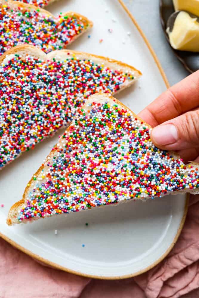 Closeup of a slice of fairy bread being picked up.