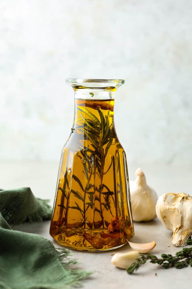 A glass jar filled with olive oil, herbs, and garlic.