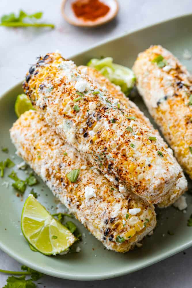 A close up of 4 Mexican grilled ears of corn on a green platter. 