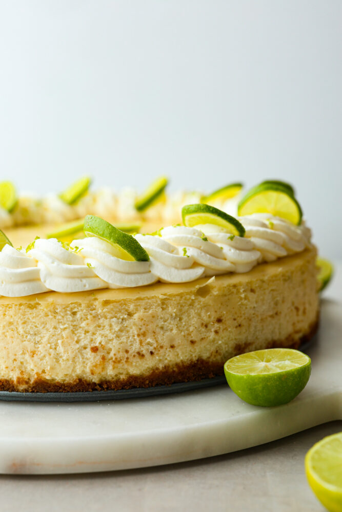 A whole cheesecake, garnished with whipped cream and sliced limes.