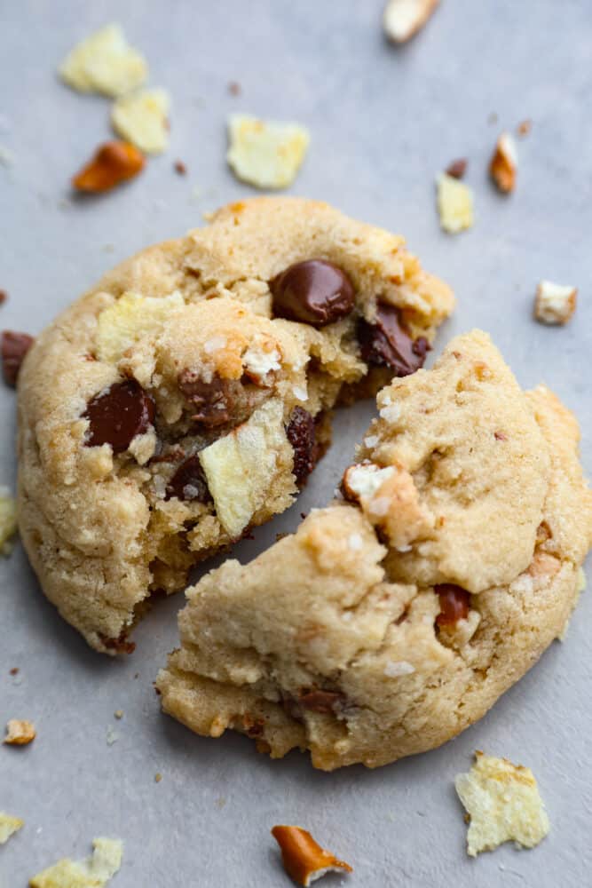 These kitchen sink cookies are the perfect chaotic blend of pretty much everything but the kitchen sink! A chocolate chip cookie is taken to the next level with pretzels, potato chips, and candy pieces. You won't be able to get over how amazing these cookies are! A kitchen sink cookie broken in half.