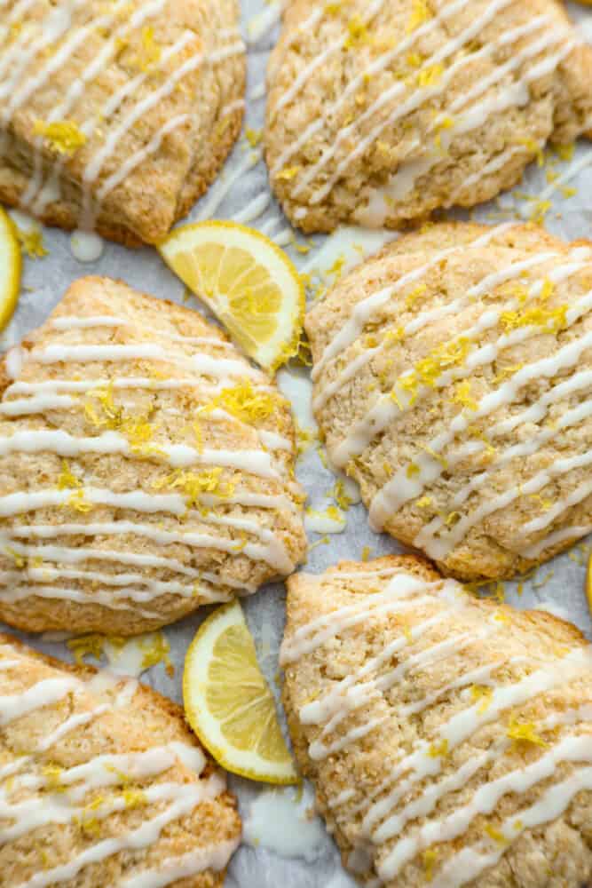 Multiple scones drizzled with icing on a baking sheet.