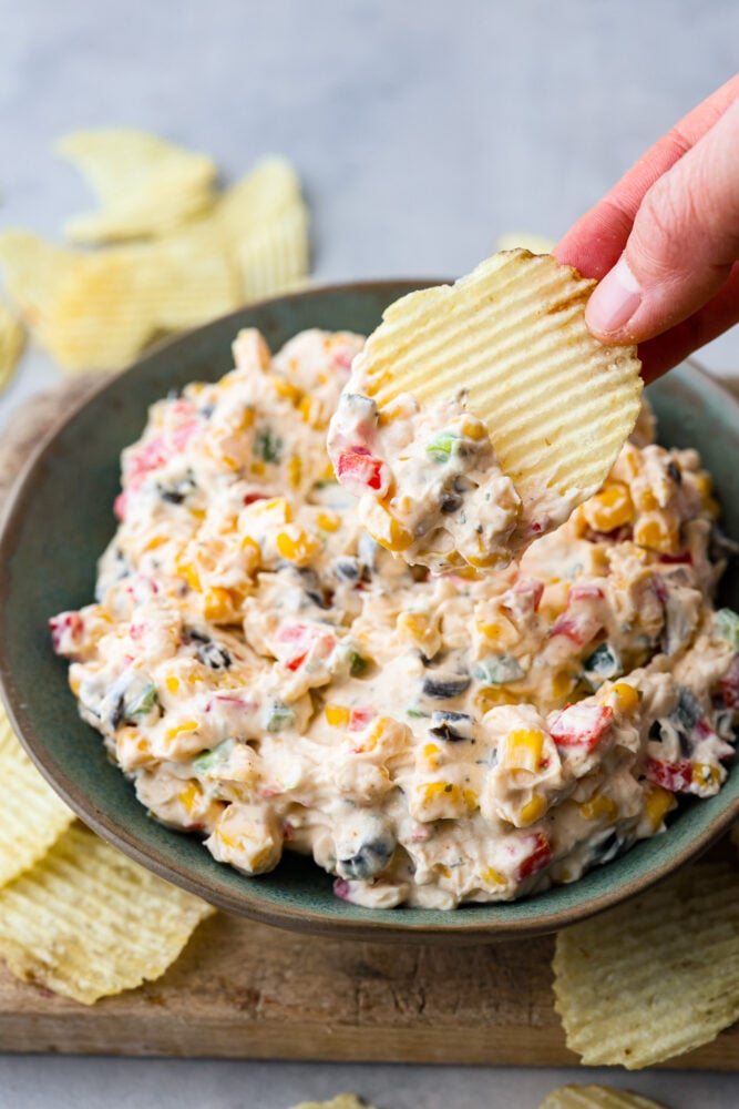 A bowl of poolside dip with a potato chip scooping some dip. 