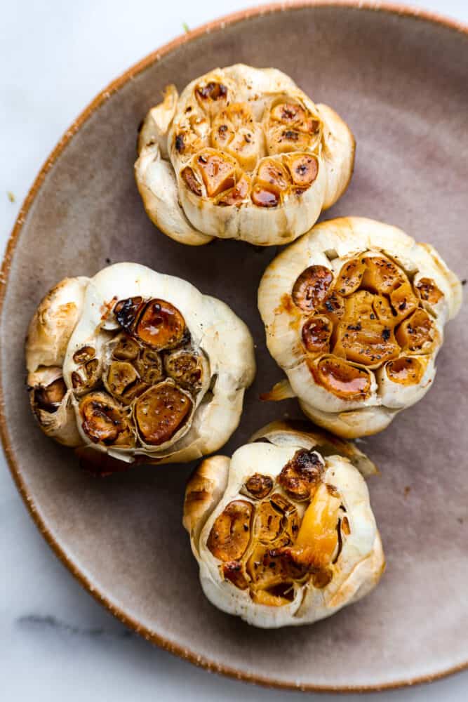 4 heads of roasted garlic in a gray dish.