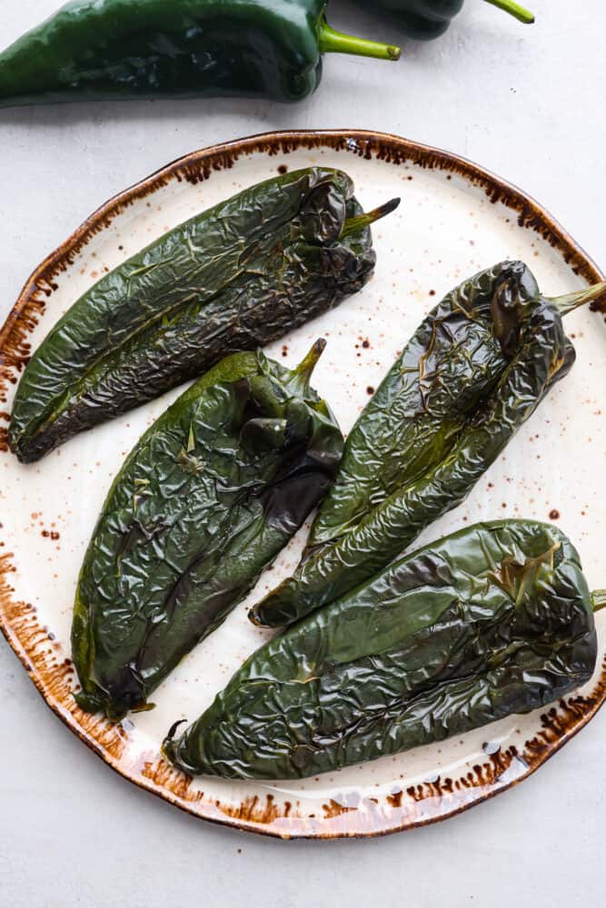 4 roasted poblano peppers on a white plate.