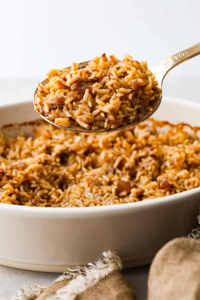 A gold spoon scooping up baked rice from a casserole dish.