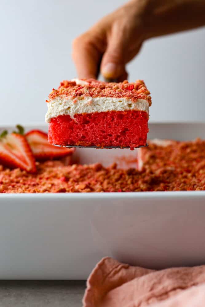 Side view of a piece of Strawberry Crunch cake being lifted out of the pan with a cake server. 