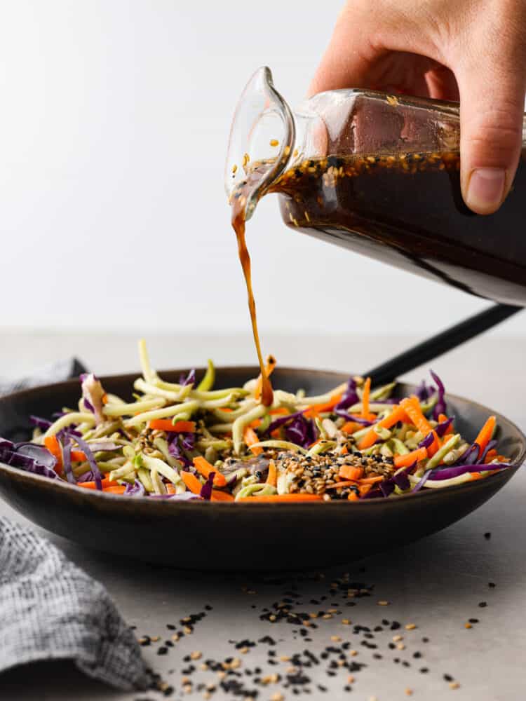 The dressing is poured over a bowl of vegetables.