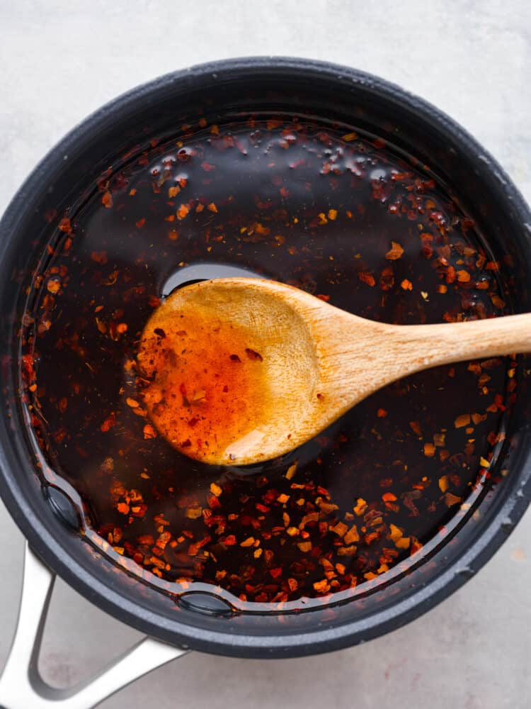 Top view of chili oil in a black saucepan. A wooden spoon is lifting out chili oil.