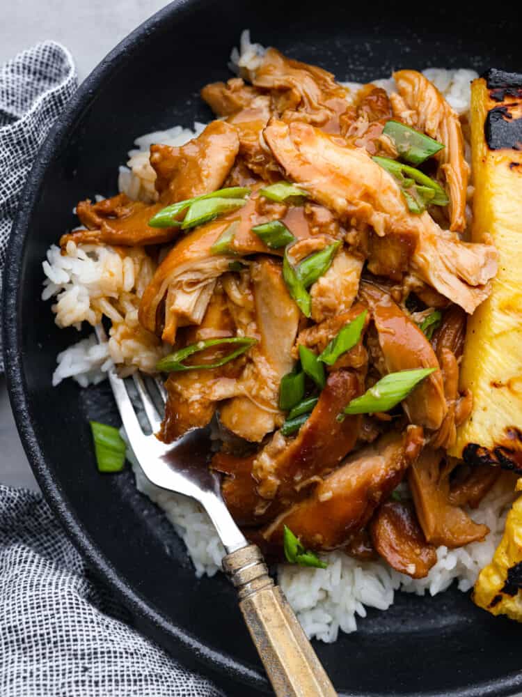 Crockpot huli huli chicken is a dinner you can set and forget, then come back to and enjoy in all of its tropical goodness! Each bite of fork-tender chicken is flavored with the best sauce made of ginger, garlic, ketchup, brown sugar, and pineapple juice. It's the perfect mix of sweet, tangy, and savory! Closeup of huli huli chicken on a black plate.