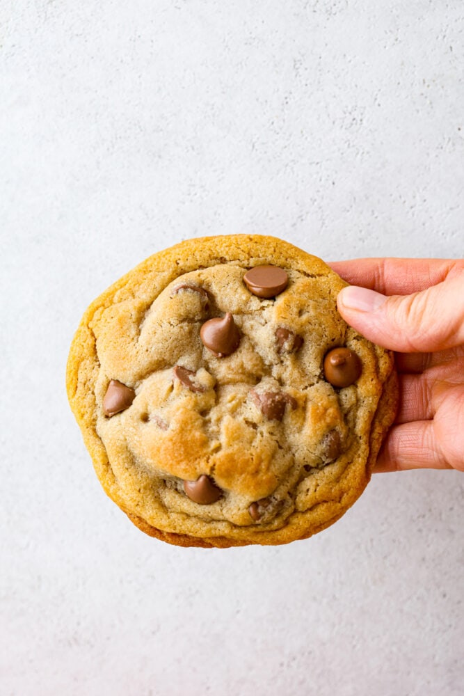 Close up view of a hand holding a large copycat Crumbl cookie.