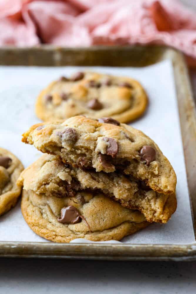 Closeup view of broke cookies stacked on top of a baking sheet pan. A pink towel is next to the pan.