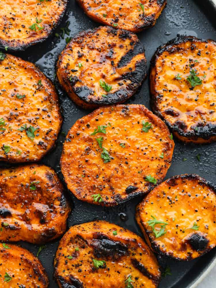 Closeup of grilled sweet potatoes, topped with seasonings and herbs.