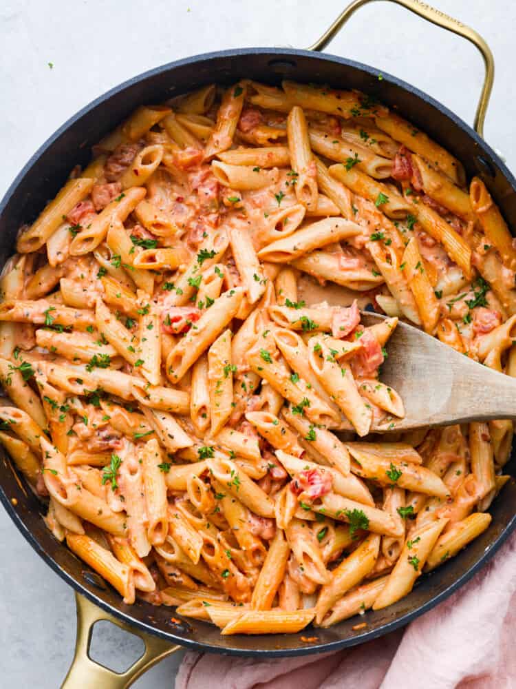 A picture of spaghetti with pink sauce in a pan with a wooden spoon. 