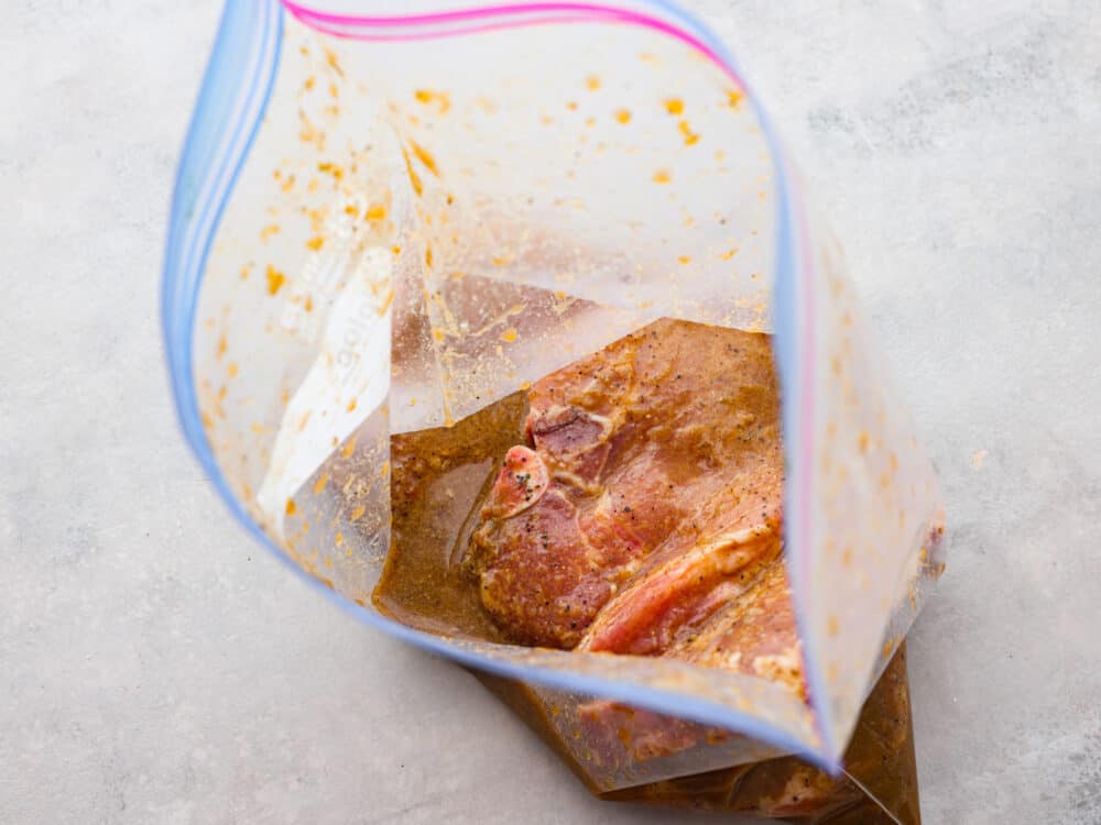 Raw pork chops added to a bag of marinade.