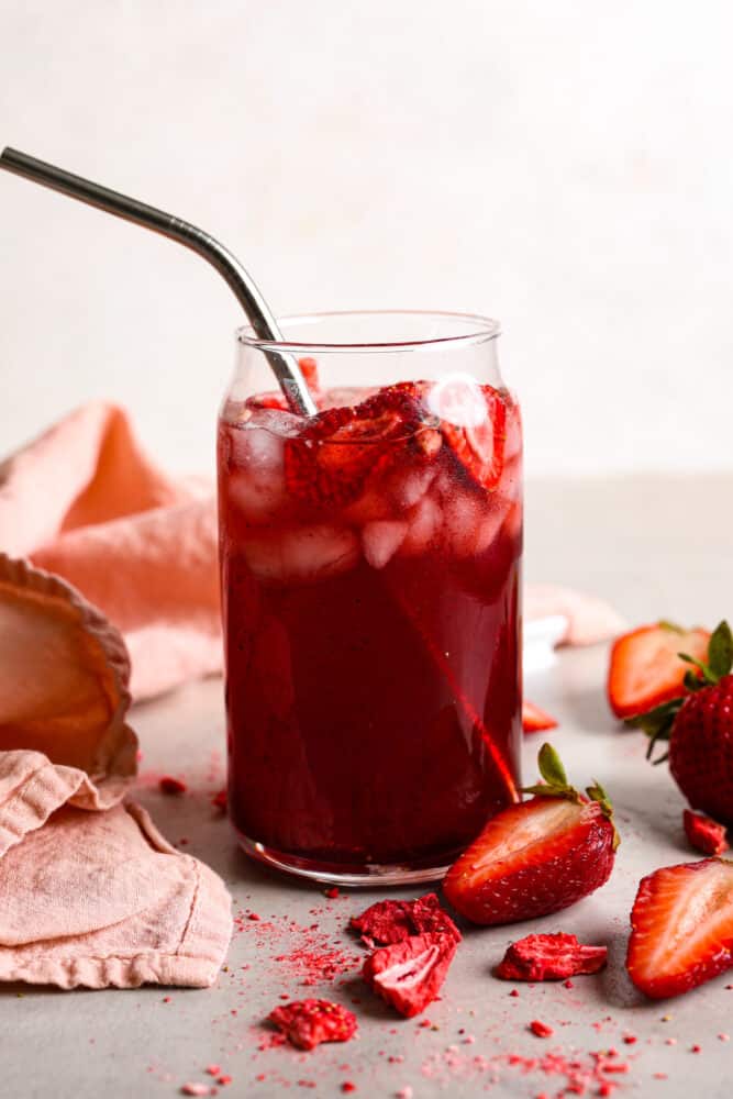 A strawberry acai refresher in a clear glass cup with a metal straw. 