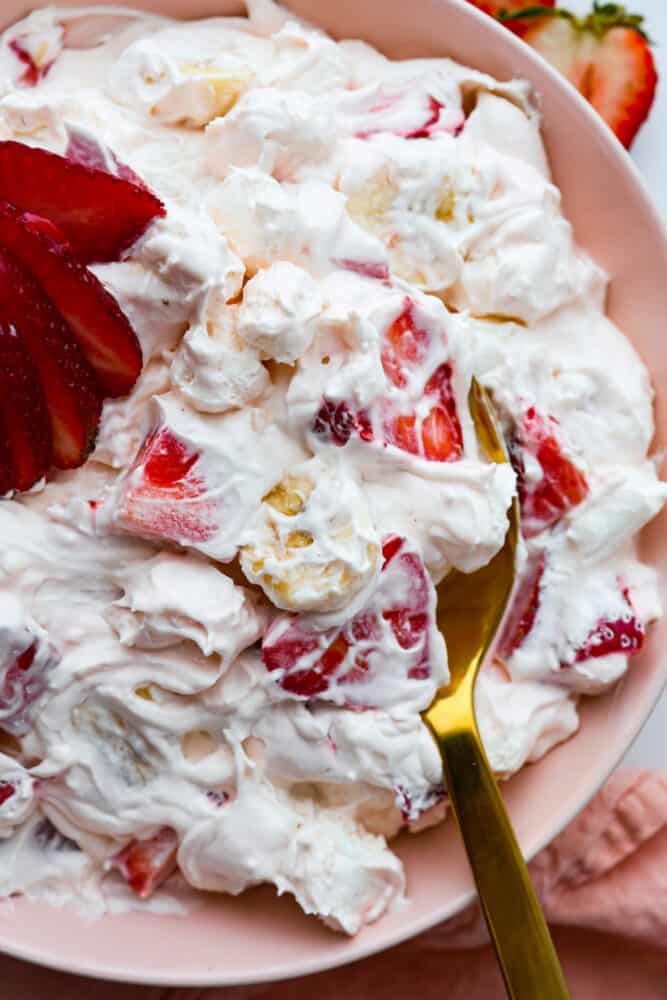 Strawberry Cheesecake Salad is a sweet and creamy dessert with fresh strawberries hidden throughout. This is the biggest hit at any potluck and SO easy to make! A spoonful of fruit salad filled with sliced strawberries and bananas.