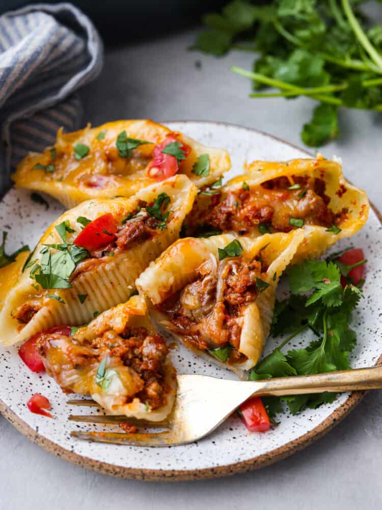 Close up view of taco stuffed shells on a plate. A gold fork is resting on the plate next to the shells.