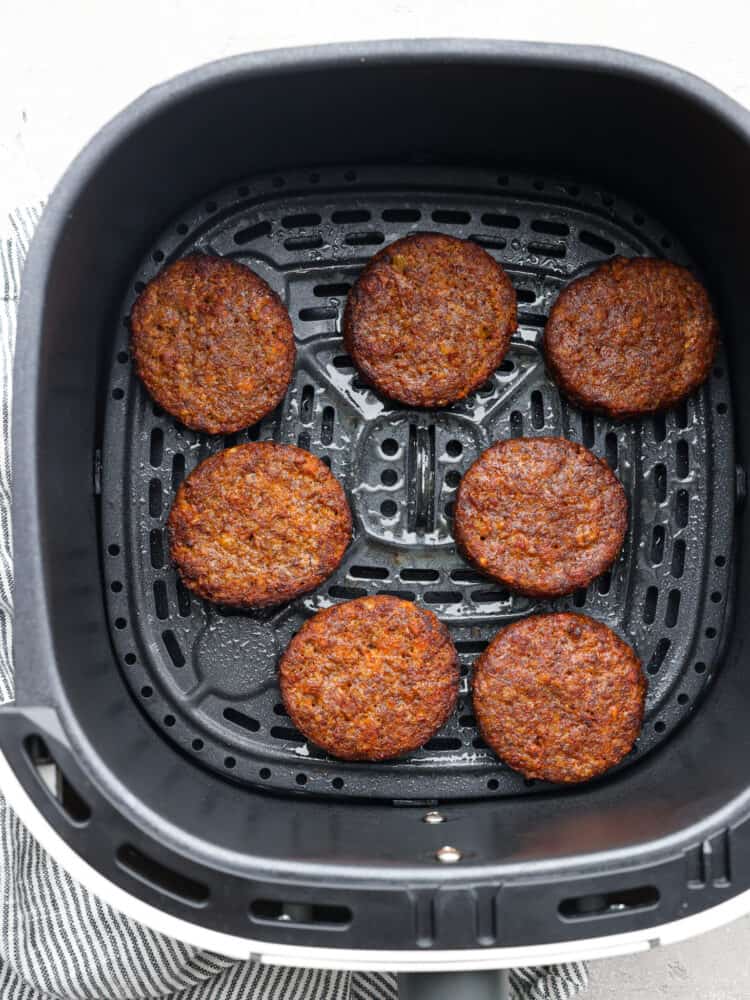 Cooked sausage patties in the basket of an air fryer.