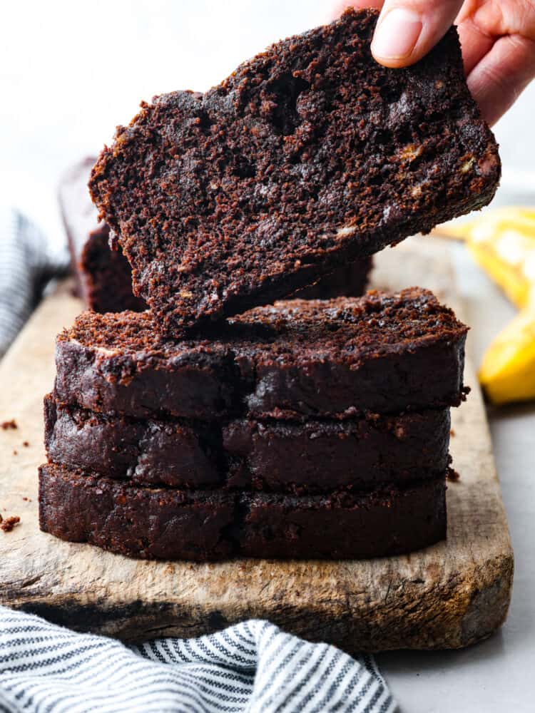 Side view of stacked slices of chocolate banana bread. A hand is lifting a slice of bread.