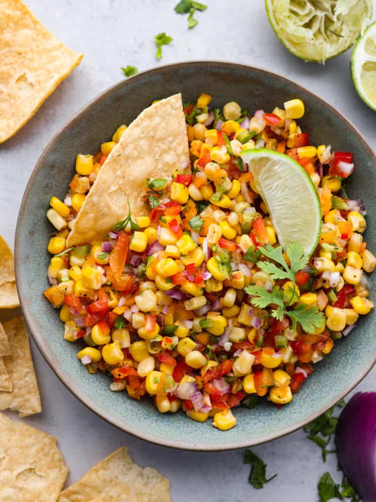 Top view of a bowl of corn salsa garnished with cilantro and topped with lime and tortilla chips. 