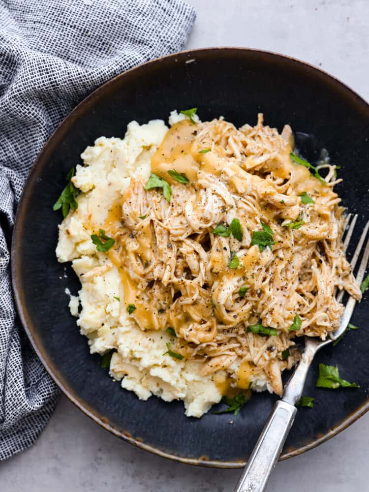 Chicken and gravy garnished with green onions on a plate with mashed potatoes.