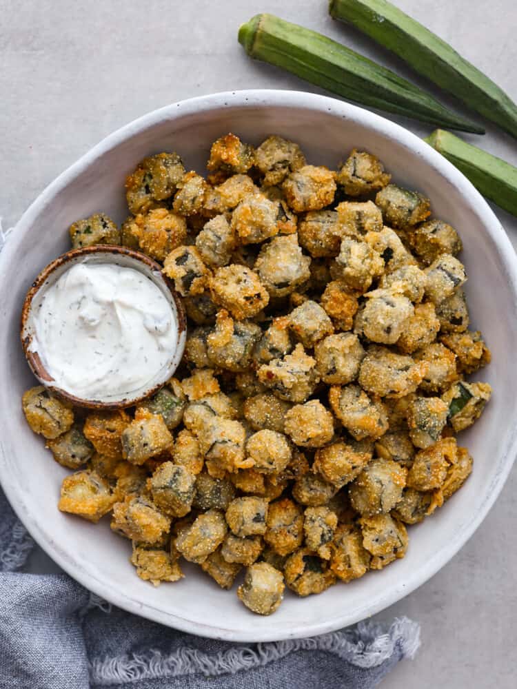 Fried okra served in a white bowl with a creamy sauce.
