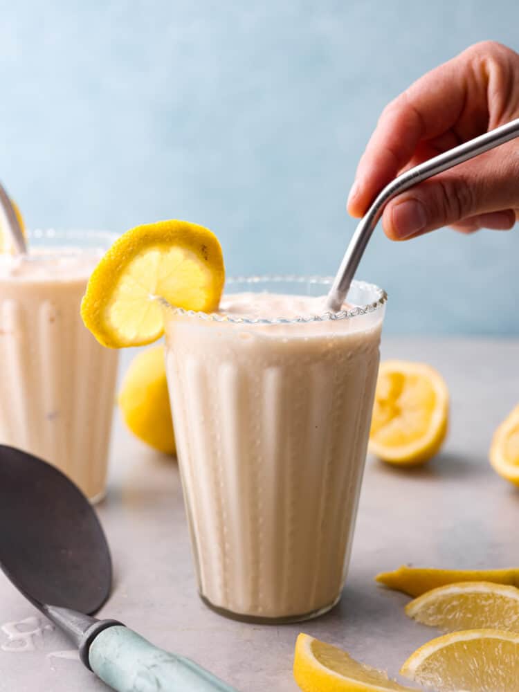 Die Seitenansicht einer gefrosteten Limonade mit einer Hand, die einen Strohhalm in das Glas steckt. 