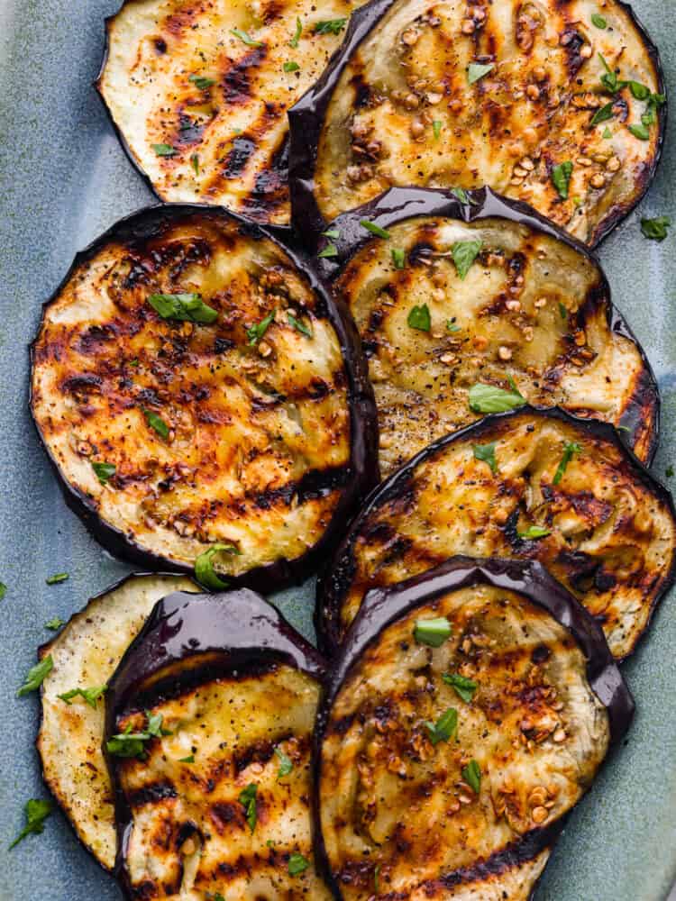 Close up view of grilled eggplant on a blue platter garnished with chopped parsley.