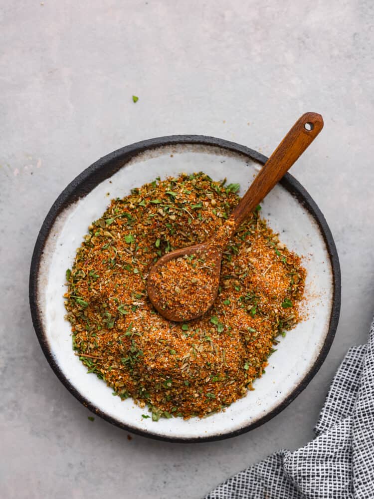 Overhead view of gyro seasoning in a white bowl and a wood spoon.