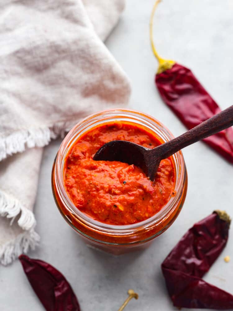 Top-down view of a jar of harissa paste with a wooden spoon inside.