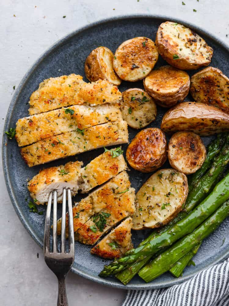 Sliced chicken, potatoes and asparagus on a blue plate with a fork on top. 