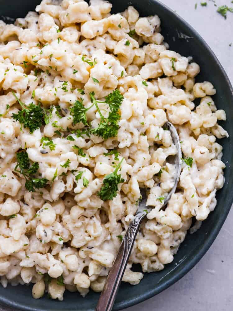 Spaetzle served with fresh herbs in a black bowl.